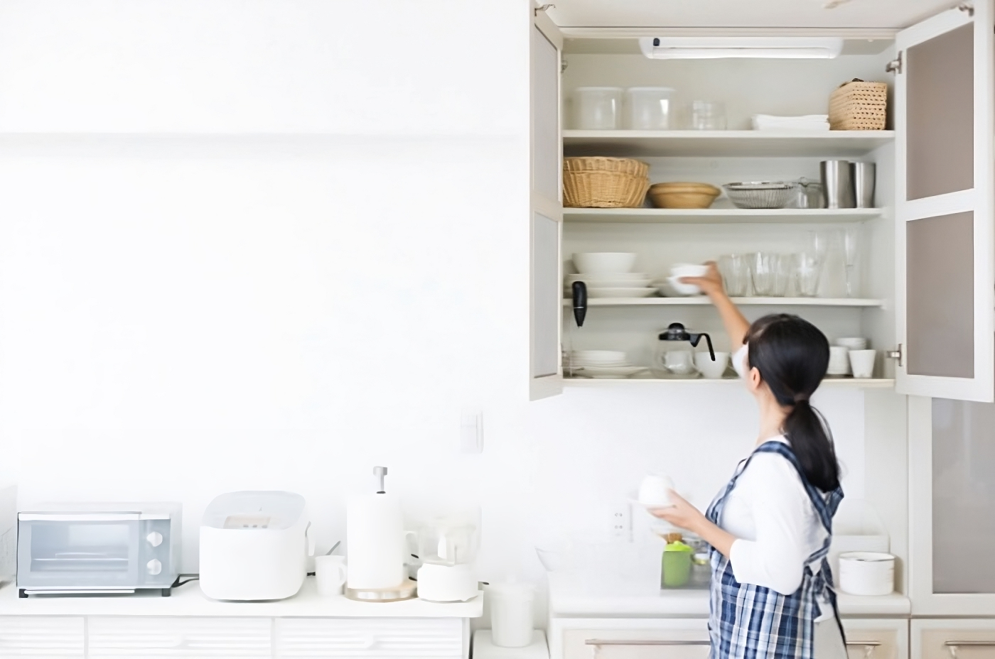 Image of Streamline striplight in a kitchen cupboard, a lady is reaching up to the cupboard to grab bowls, the automatic door switch turns the light on.