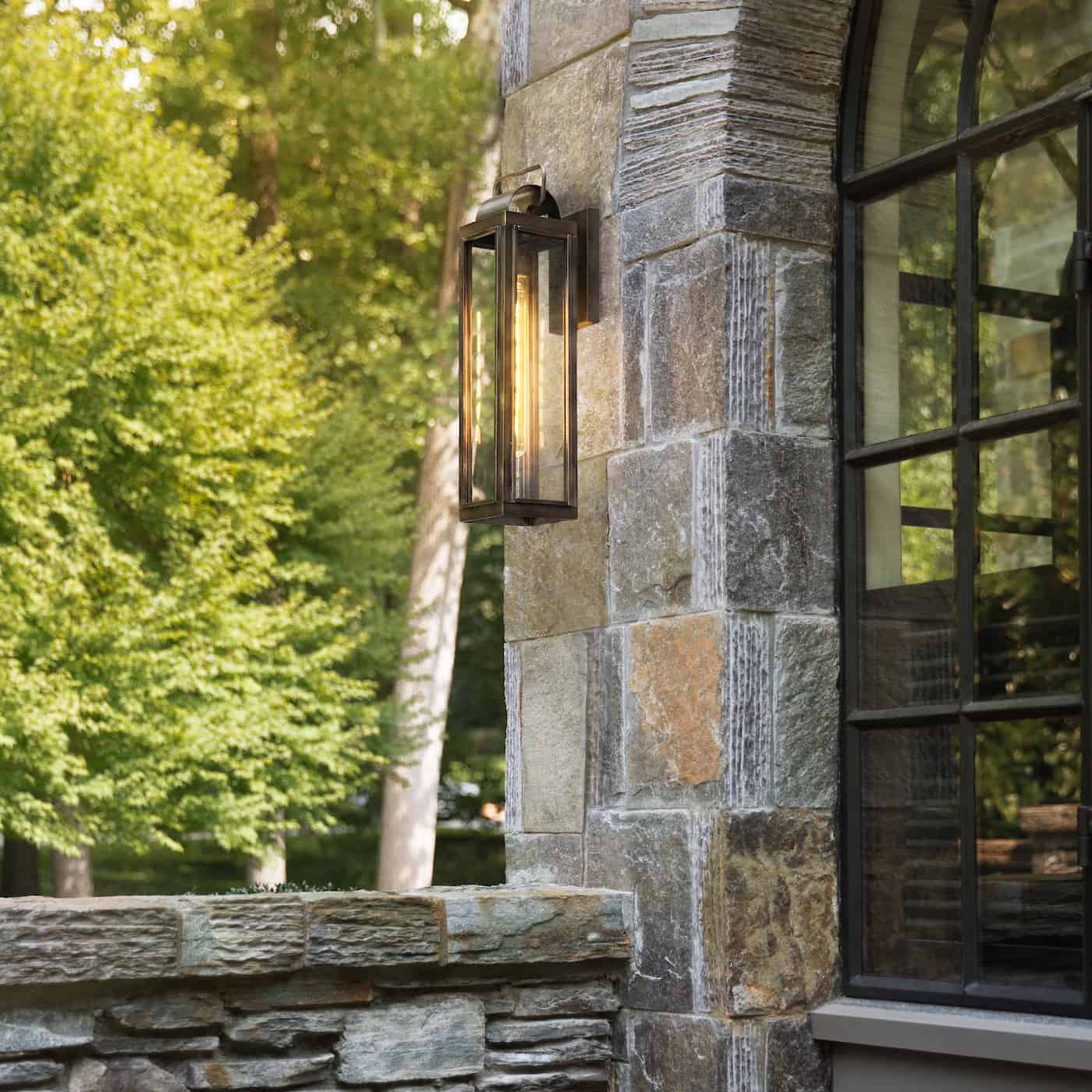 a sag harbour wall lantern mounted on the stone exterior wall of a home with a window nearby