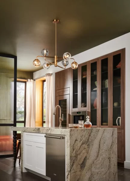 a multi-coloured oberon pendant from hinkley lighting hangs over a modern kitchen island in a darkly decorated room